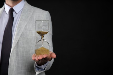 Closeup view of businessman holding hourglass on black background, space for text. Time management