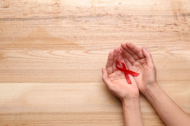Photo of Woman holding red awareness ribbon on wooden background, top view with space for text. World AIDS disease day