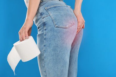 Woman with toilet paper suffering from hemorrhoid on light blue background, closeup