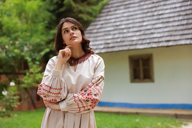 Beautiful woman wearing embroidered dress in village, space for text. Ukrainian national clothes