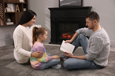 Happy family reading book together on floor near fireplace at home