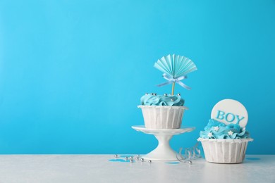 Baby shower cupcakes with toppers on white table against light blue background, space for text