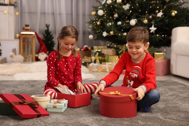 Cute little children with gift boxes near Christmas tree at home