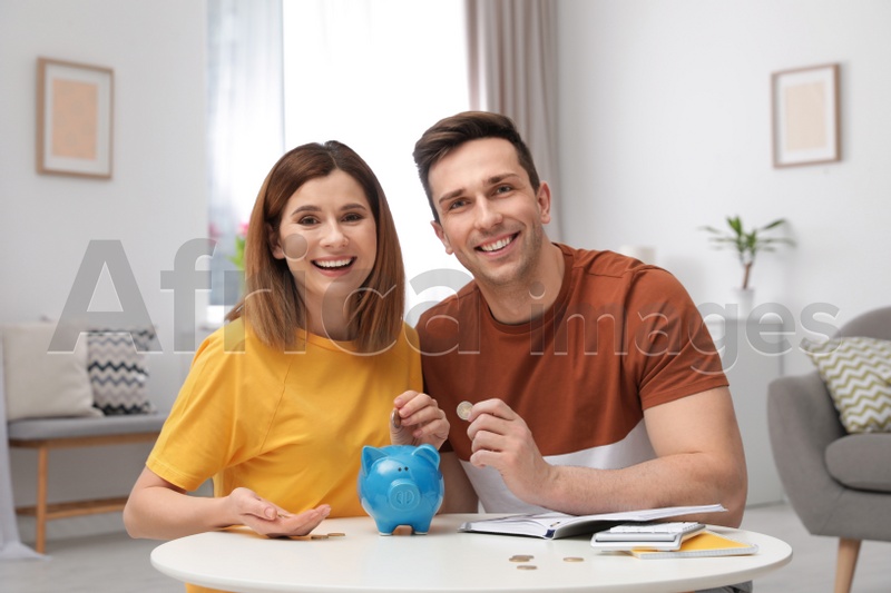 Couple putting coins into piggy bank at table in living room. Saving money