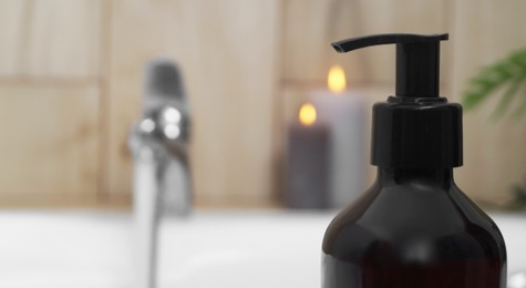 Black bottle of bubble bath on tub indoors, closeup. Space for text