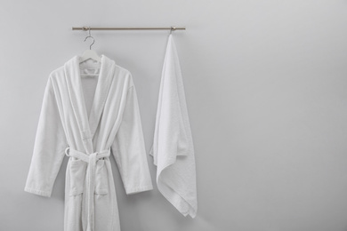 Hanger with clean bathrobe and towel on light wall. Space for text