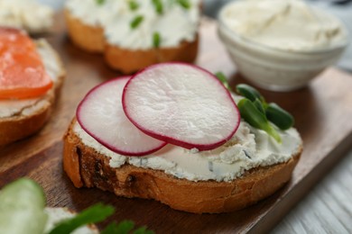 Toasted bread with cream cheese, radish and microgreen on wooden board, closeup
