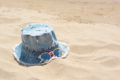 Photo of Jeans hat and sunglasses on sand, space for text. Beach accessories