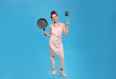Housewife with frying pan and spatula on light blue background