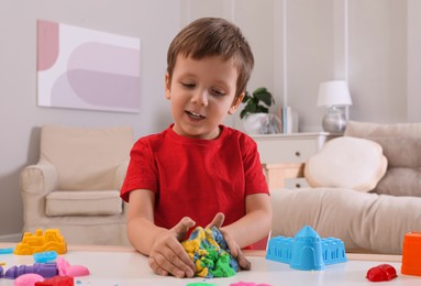 Cute little boy playing with bright kinetic sand at table in room
