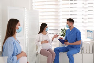 Doctor consulting patient while other pregnant woman waiting for appointment in clinic