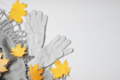 Stylish woolen gloves, scarf and dry leaves on white background, top view
