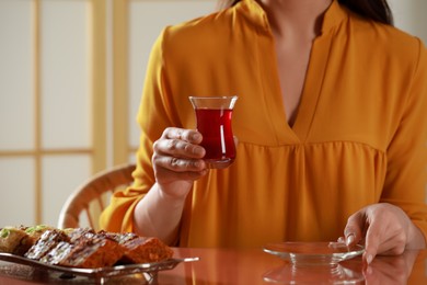 Photo of Woman holding glass of traditional Turkish tea at table indoors, closeup