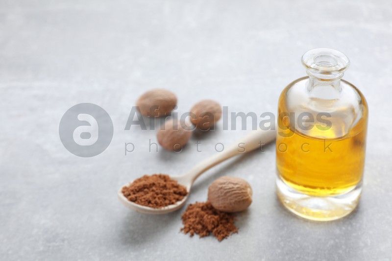 Photo of Bottle of nutmeg oil, nuts and powder on light grey table, closeup. Space for text
