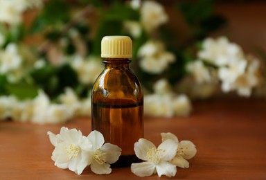 Bottle of jasmine essential oil and beautiful flowers on wooden table, closeup