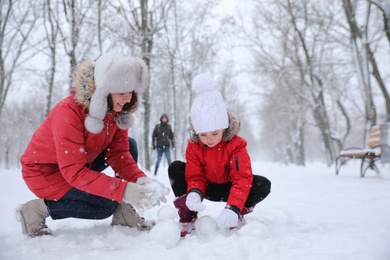 Mother with her child building small snowman outside on winter day. Christmas vacation