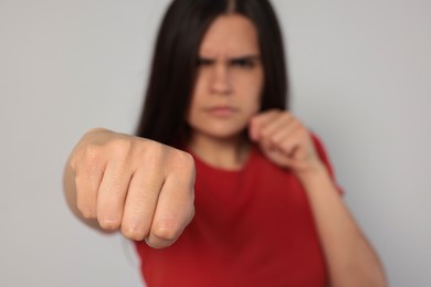 Young woman ready to fight against light grey background, focus on hand. Space for text