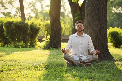 Man meditating in park on sunny summer day. Space for text