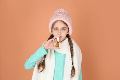 Sick little girl using nasal spray on coral background