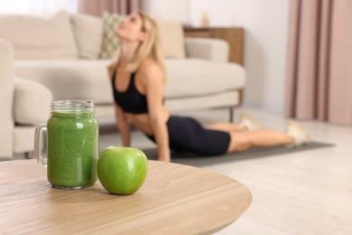 Photo of Young woman in fitness clothes exercising at home, focus on mason jar of smoothie and apple