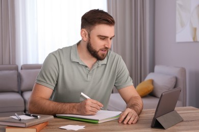 Young man taking notes during online webinar at table indoors