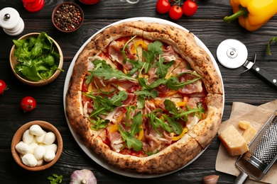 Tasty pizza with meat and arugula on black wooden table, flat lay