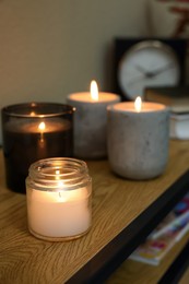 Lit candles in different holders on wooden table indoors. Space for text