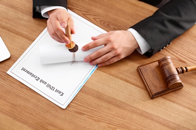 Male notary sealing document at wooden table, closeup