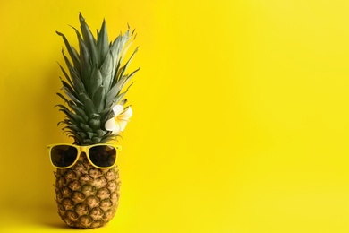 Photo of Funny pineapple with sunglasses and plumeria flower on yellow background, space for text. Creative concept