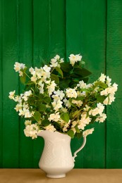 Bouquet of beautiful jasmine flowers in vase on wooden table