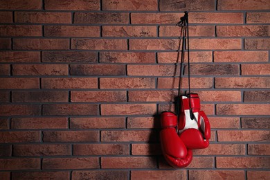 Pair of red boxing gloves hanging on brick wall, space for text