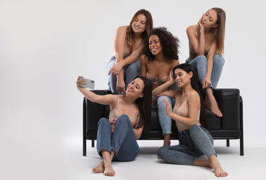 Group of women with different body types in jeans and underwear taking selfie against light background
