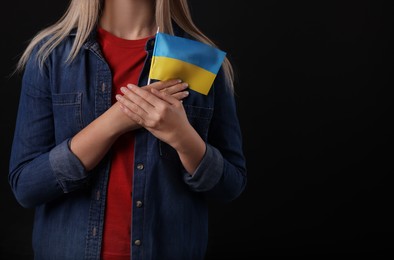 Photo of Woman holding Ukrainian flag on black background, closeup. Space for text