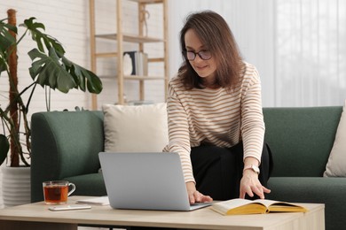 Woman with modern laptop and book learning in living room