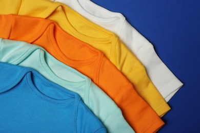 Closeup of cute baby onesies on color background, top view