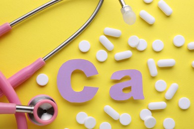 Photo of Stethoscope, pills and calcium symbol made of purple letters on yellow background, flat lay