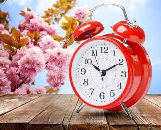 Red alarm clock on wooden table. Daylight saving time (Spring forward)