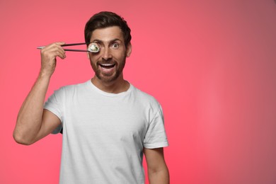 Photo of Funny man hiding his eye with tasty sushi roll on pink background. Space for text