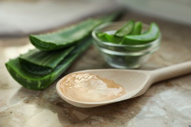 Green aloe vera leaves and spoon of gel on table, closeup