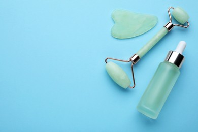 Jade gua sha tool, facial roller and bottle of serum on light blue background, flat lay. Space for text