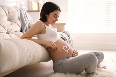 Young pregnant woman with cosmetic product on belly at home