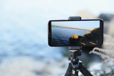 Photo of Tripod with smartphone on river coast, closeup. Space for text