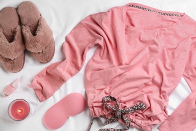 Flat lay composition with fluffy slippers and pajamas on white bedsheet. Comfortable home outfit