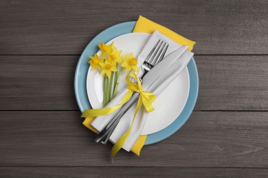 Photo of Festive table setting with narcissuses and cutlery on wooden background, top view. Easter celebration