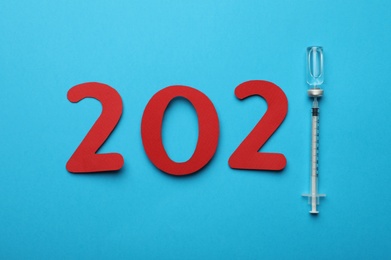 Paper numbers, syringe and vial with coronavirus vaccine forming 2021 on light blue background, flat lay