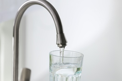 Filling glass with clear water from faucet on light background, closeup