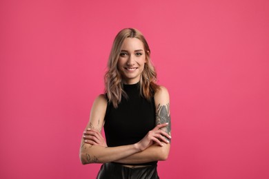 Beautiful woman with tattoos on arms against pink background