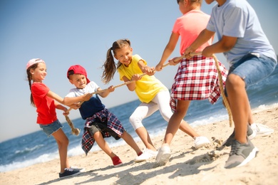 Cute children pulling rope during tug of war game on beach. Summer camp
