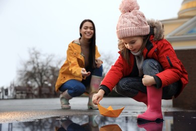 Little girl and her mother playing with paper boat near puddle outdoors