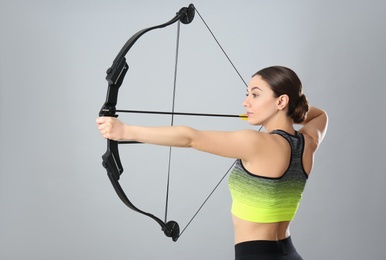 Sporty young woman practicing archery on light grey background